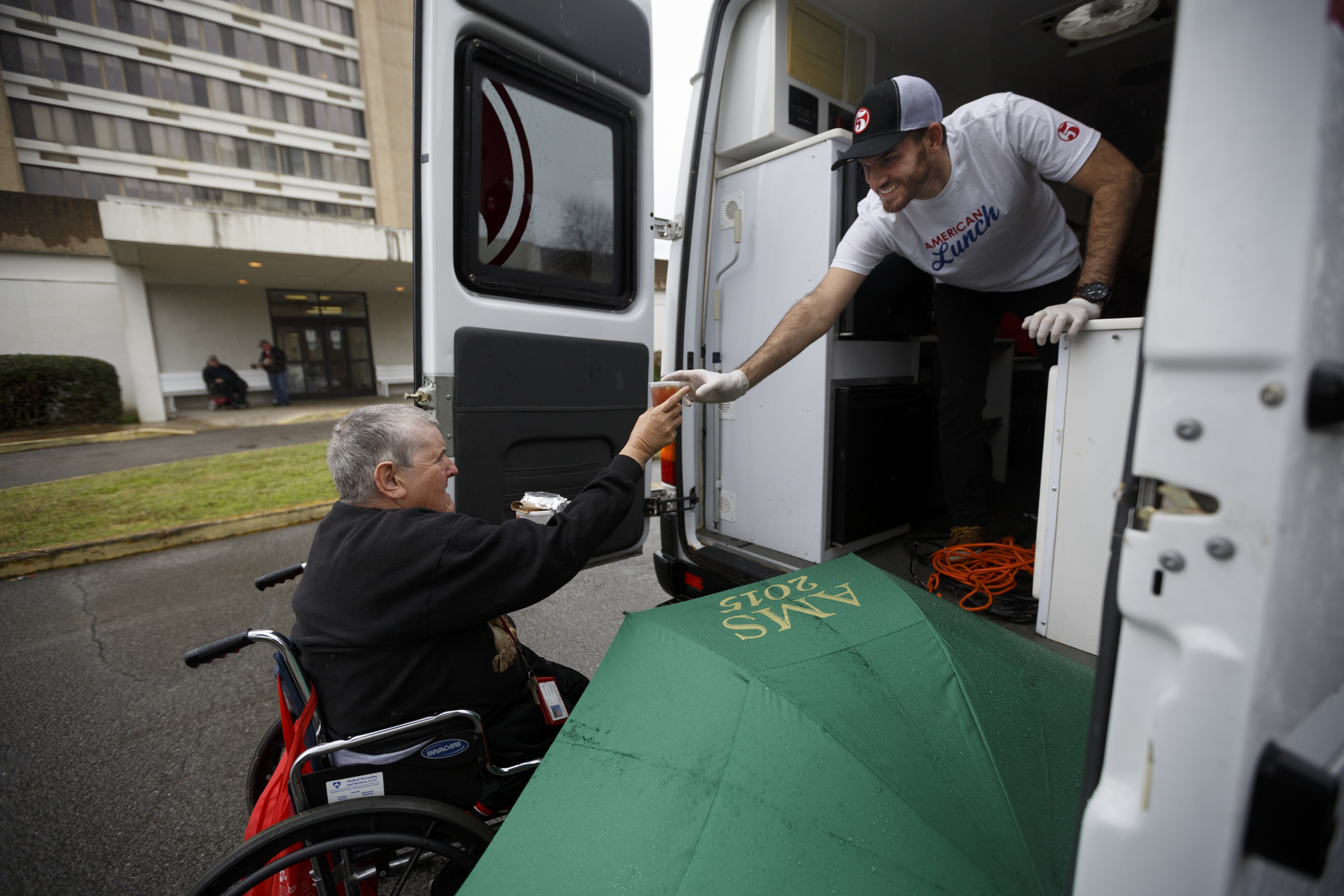 Staff photo by Doug Strickland / Nate Brown, right, hands a cup of tea to Brenda Smith from the food truck near the Boynton Terrace Apartments. Beginning last September, the restaurant Five Bar began serving free lunches at the Boynton Terrace apartments out of its food truck on Mondays, Wednesdays, and Fridays.