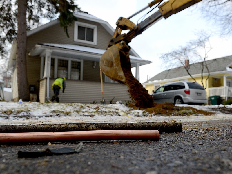 As the hole is filled in in the background, a piece of an old lead water pipe sits next to a new copper pipe, Friday, Jan. 22, 2016, at a home on Greencroft in Lansing, Mich. Lansing's municipal utility says it's nearly eliminated lead water service lines since concerns in 2004 prompted it to launch a massive program to replace them with copper lines by 2017. (Dave Wasinger/Lansing State Journal via AP)