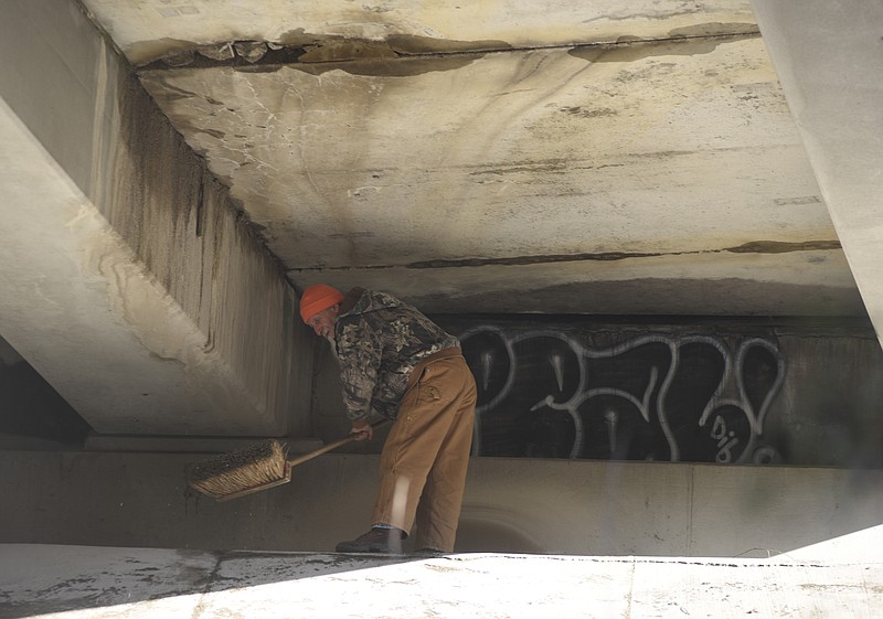 A TDOT worker clears away debris underneath an I-24 overpass in between Broad Street and the Highway 27 split on Sunday, Jan. 24, 2016, in Chattanooga, Tenn. According to TDOT, one eastbound lane will be closed until bridge workers can make repairs after workers fixing potholes found a broken deck panel and slab on the bridge.