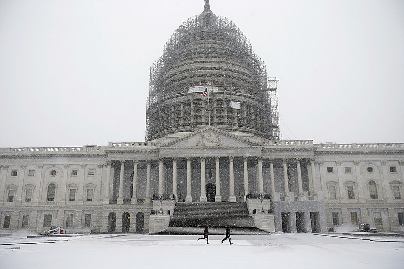 
              Two runners jog as the snow falls on Capitol Hill, Friday, Jan. 22, 2016, in Washington. One in seven Americans will get at least half a foot of snow outside their homes when this weekend's big storm has finished delivering blizzards, gale-force winds, whiteout conditions and flooding to much of the eastern United States. (AP Photo/Alex Brandon)
            