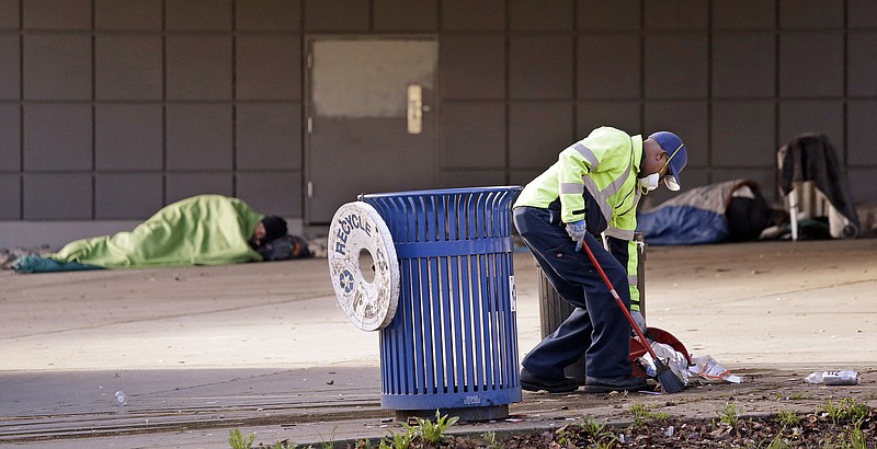 
              A contract worker cleans-up trash as men continue to sleep behind him under an overpass near where police arrested three teenage boys the day before in connection with a January shooting at a Seattle homeless encampment known as 'The Jungle' that left 2 people dead and three others wounded, Tuesday, Feb. 2, 2016, in Seattle. (AP Photo/Elaine Thompson)
            