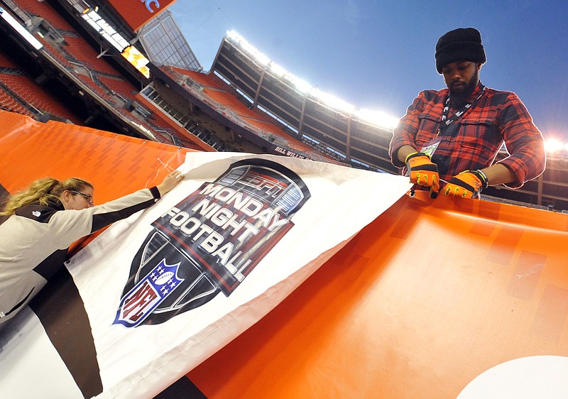 
              FILE - In this Nov. 3, 2015, file photo, workers install an ESPN Monday Night Football banner before an NFL football game between the Cleveland Browns and the Baltimore Ravens in Cleveland. The sports network that drives Disney’s profit engine has hit a soft patch as people cut the cord to watch programming online. It's a sign of one of TV’s biggest challenges: the ever-increasing cost of sports rights and whether consumers want to keep footing the bill. (AP Photo/David Richard, File)
            