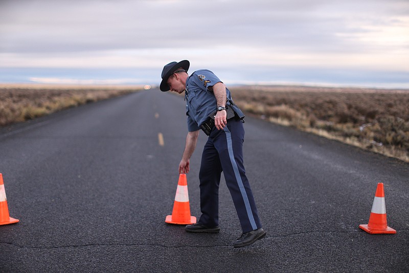 
              FILE -In a Jan. 28, 2016 file photo, an officer with the Oregon State Police moves a cone to establish a roadblock along one of the routes to the Malheur National Wildlife Refuge in Harney County, Ore. The FBI said Wednesday, Feb. 10, 2016, that it has moved to contain the last few occupiers of an Oregon wildlife refuge who were part of a protest that began more than a month ago over federal land policy. (Beth Nakamura/The Oregonian via AP, File) MANDATORY CREDIT
            