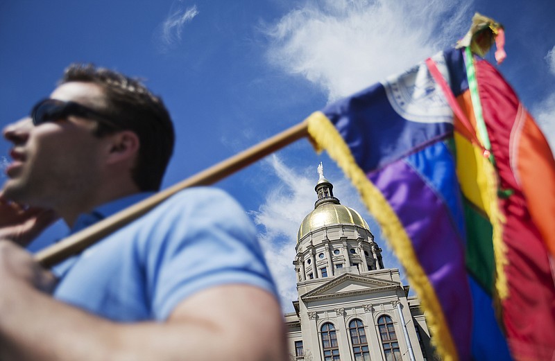 In this March 17, 2015, file photo, the dome of the Capitol stands in the background as Stephen Saras, of Atlanta, holds a rainbow-colored flag during a rally against a contentious "religious freedom" bill in Atlanta. (AP Photo/David Goldman, File)