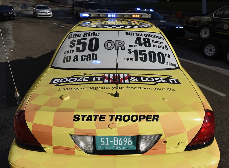 A sign comparing the costs of a taxi ride and a DUI conviction is seen on the back window of a Tennessee Highway Patrol vehicle painted to resemble a taxi during a news conference with members of the Chattanooga Police Department, Hamilton County Sheriff's Office and Georgia State Patrol on Monday, Dec. 7, 2015, in Chattanooga, Tenn., discussing DUI enforcement efforts during the holiday season. 