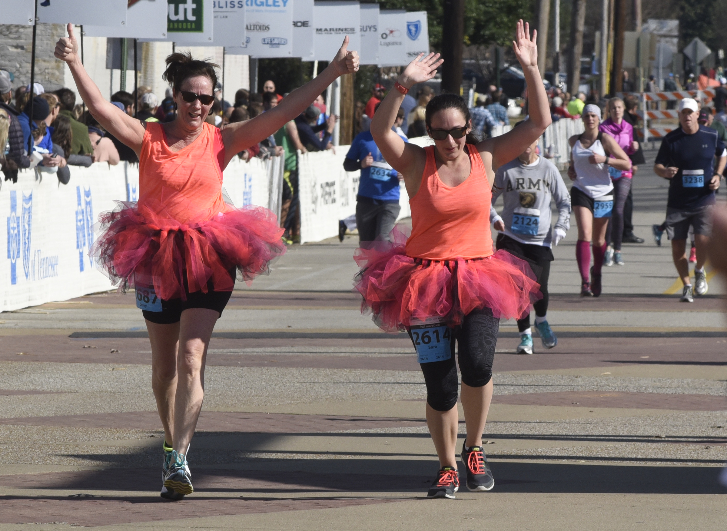 Dressed in matching tutus, Derry Micale, left, and Sara Linnertz from Syracuse, N. Y., raise their arms as the cross the finish line at the Chattanooga Marathon on Sunday, Mar. 6, 2016, in Chattanooga, Tenn.
