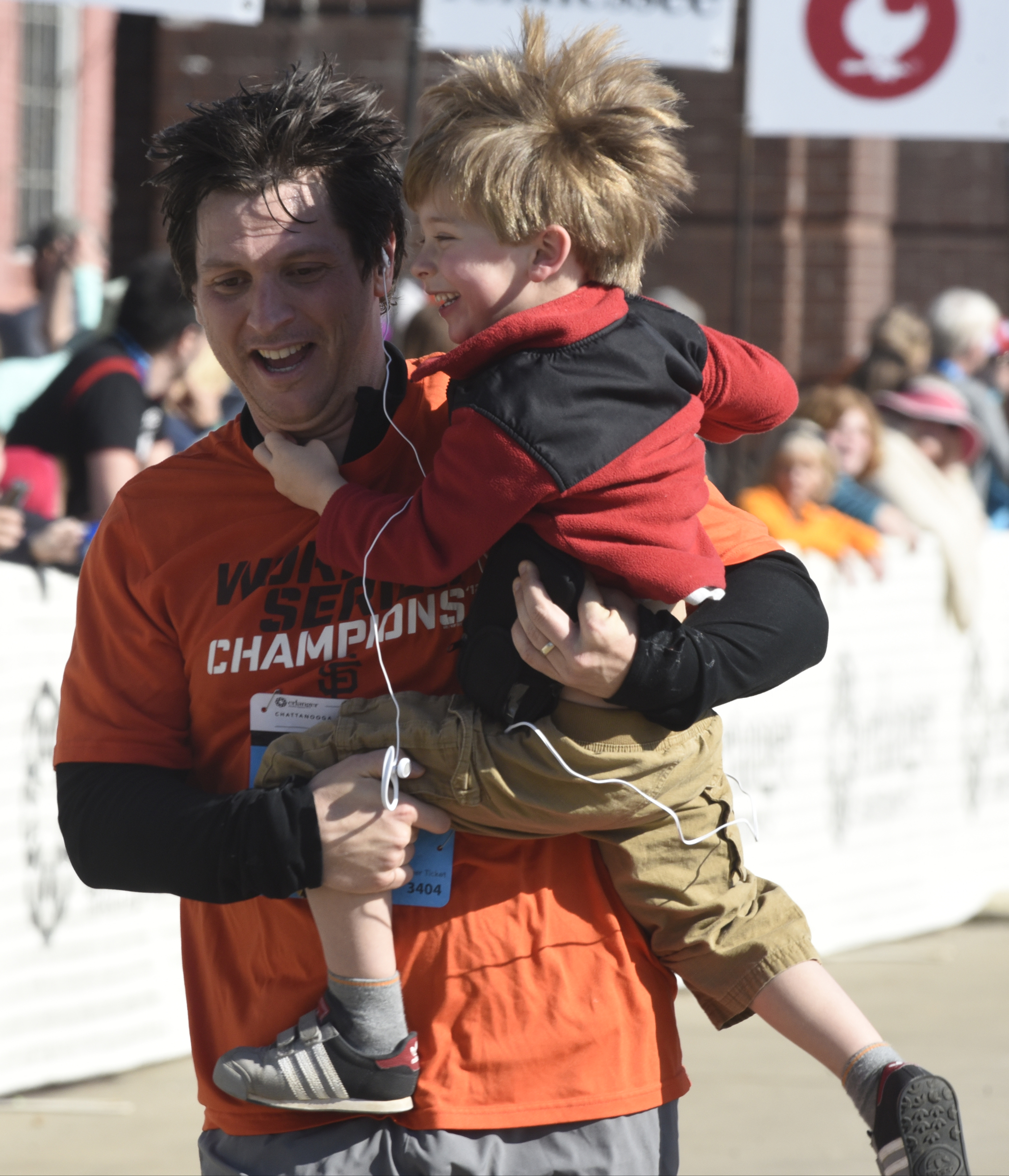 Brian Robinson of Atlanta carries his young son across the finish line at the first running of the Chattanooga Marathon on Sunday, Mar. 6, 2016, in Chattanooga, Tenn.