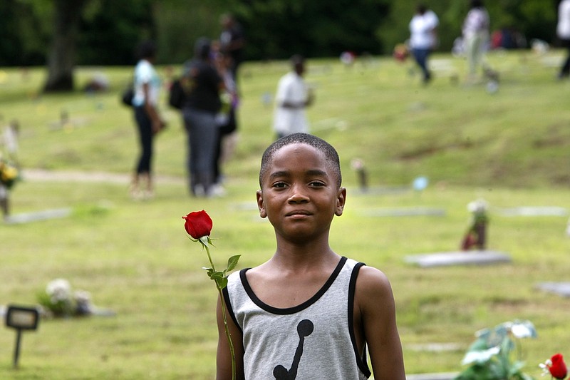 
              ADVANCE FOR USE MONDAY, APRIL 11, 2016 AND THEREAFTER - In this Monday, May 25, 2015 photo, Kendrick Cloyd, 8, holds a rose as he looks for the graves of his uncle and his sister at the Galilee Memorial Gardens cemetery in Memphis, Tenn. The cemetery was temporarily opened to visitors on Memorial Day. It was closed in 2014 after owner Jemar Lambert was accused of misplacing hundreds of bodies, burying multiple cadavers in the same grave, and crushing caskets to fit them into single plots. (AP Photo/Karen Pulfer Focht)
            