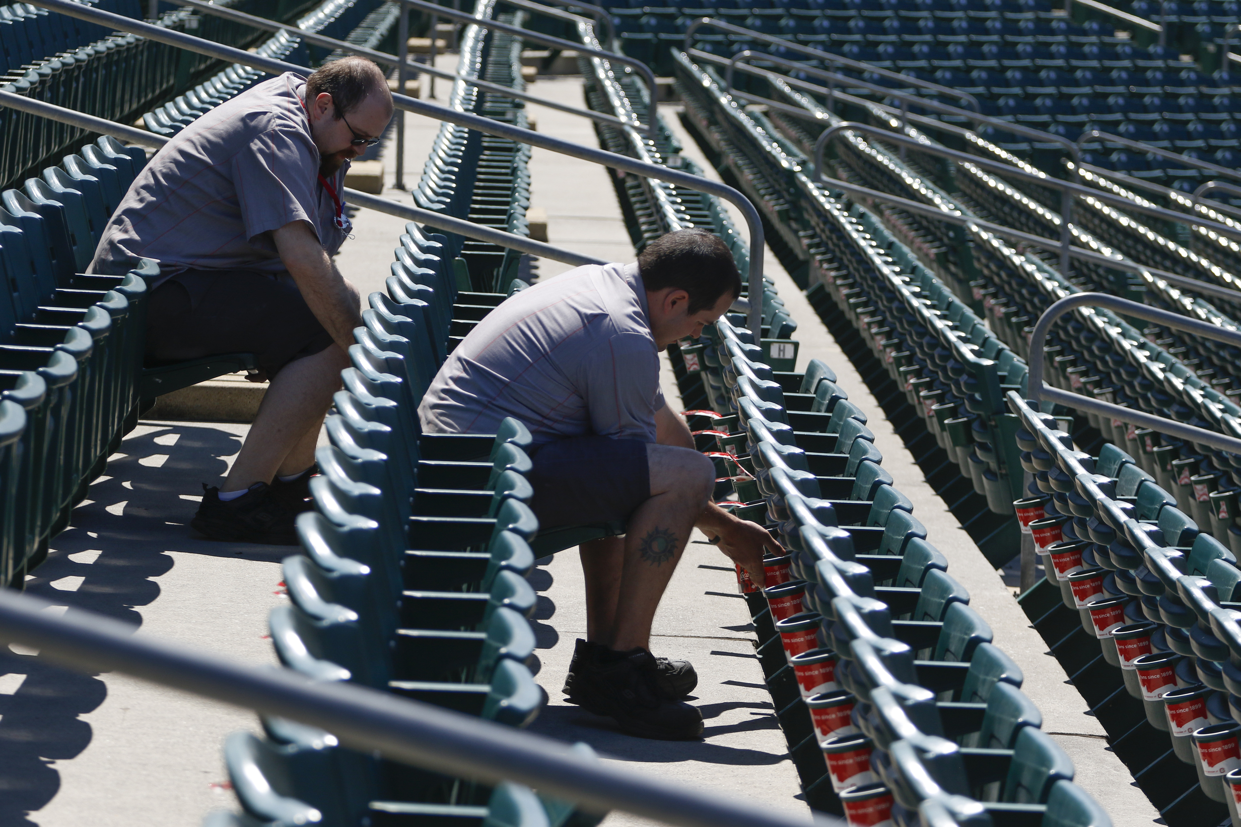 Staff Photo by Dan Henry / The Chattanooga Times Free Press- 4/5/16. Employees with CocaCola, Jeremy Culbert, left, and Mat Shelby affix new cupholder stickers on the bleachers at AT&T field on April 5, 2016.