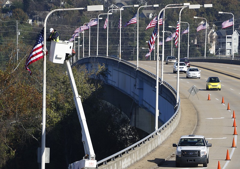 Staff Photo by Dan Henry / The Chattanooga Times Free Press- 11/11/15. Eddie Poe installs the final flag during a flag raising ceremony in the Bluff View River Gallery Sculpture Garden in honor of Veterans Day on Wednesday, November 11, 2015. Five flags will be permanently flown on Veteran's Bridge in honor of the military personnel lost earlier this year.