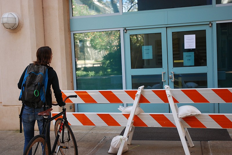 
              FILE - This March 17, 2016, file photo shows a woman reading a sign informing people that a building was closed on the University of Hawaii at Manoa campus in Honolulu after an explosion in a lab. A visiting researcher who lost an arm in a laboratory explosion last month told Honolulu fire investigators the blast occurred after she turned off a digital pressure gauge she was using to check the pressure in a gas cylinder. A report released by the Honolulu Fire Department on Monday, April 18, said the researcher told investigators she didn't hear gas leaking before the explosion. (AP Photo/Audrey McAvoy, File)
            