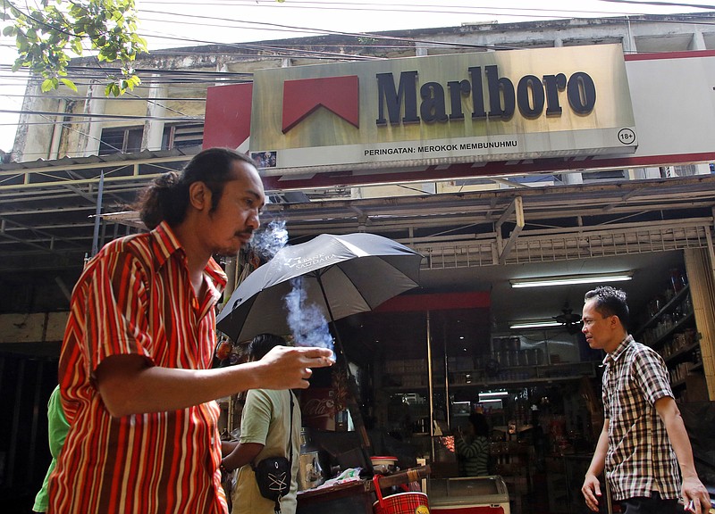 
              FILE - In this Feb. 5, 2015, file photo, a man smokes a cigarette as he walks past a shop displaying a Marlboro sign at a market in Jakarta, Indonesia. Philip Morris International reports financial results Tuesday, April 19, 2016. (AP Photo/Dita Alangkara, File)
            