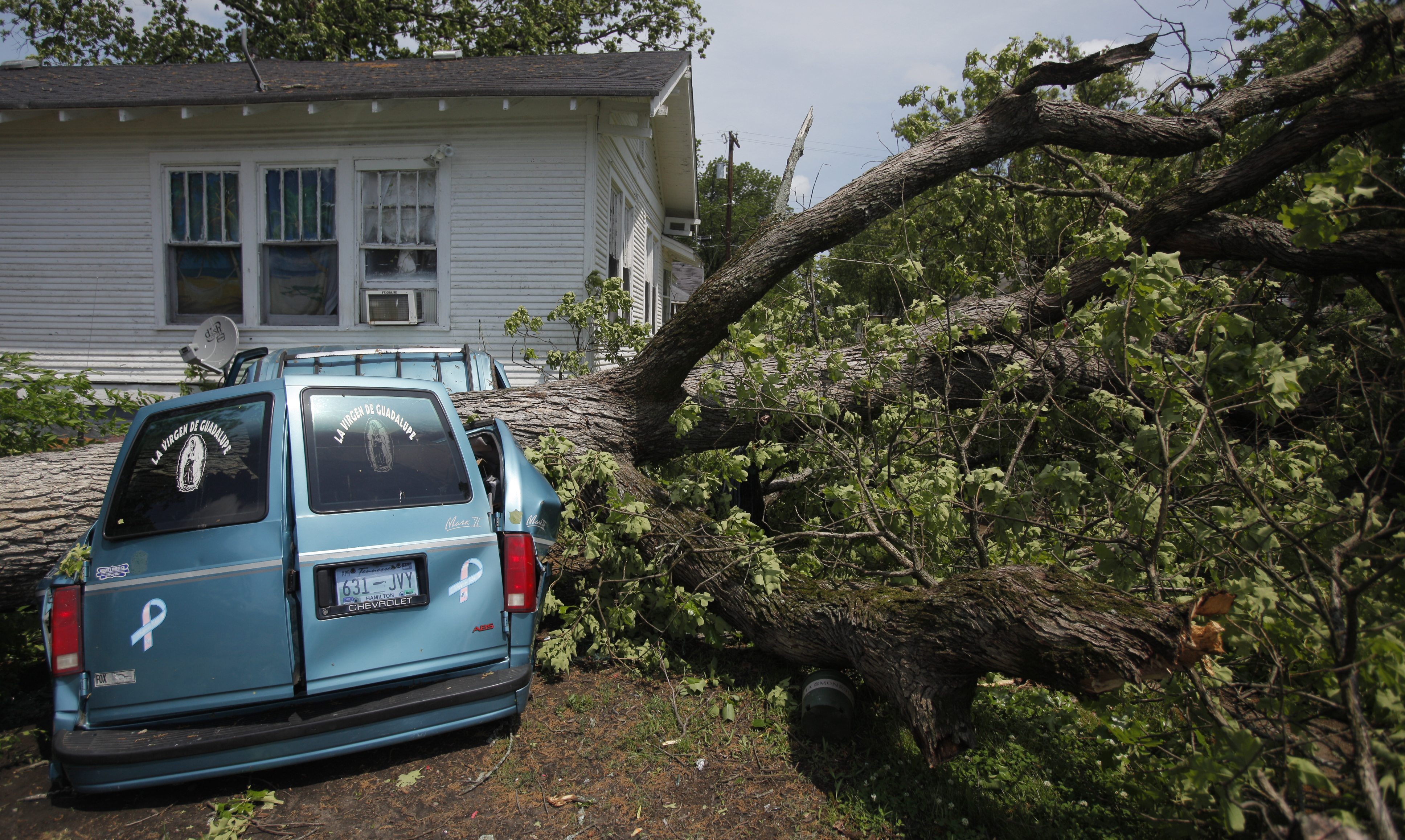A van sits crushed under the trunk of fallen tree. Trees were felled in the Highland Park neighborhood during Wednesday morning's storm.