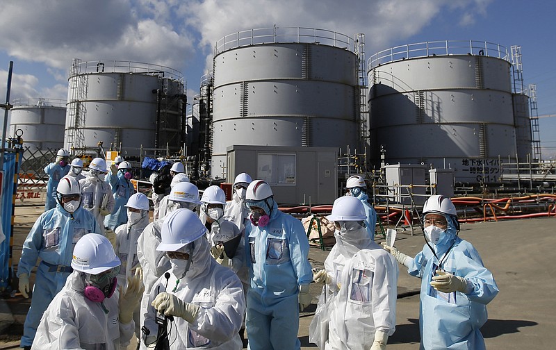 
              FILE - In this Feb. 10, 2016, file photo, members of a media tour group wearing a protective suit and a mask walk together after they receive a briefing from Tokyo Electric Power Co. employees (in blue) in front of storage tanks for radioactive water at the tsunami-crippled Fukushima Dai-ichi nuclear power plant in Okuma, Fukushima Prefecture, northeastern Japan. In an AP interview, a chief architect of an “ice wall” being built into the ground around the broken Fukushima nuclear plant defends the project but acknowledges it won’t be watertight, and as much as 50 tons of radiated water will still accumulate each day. TEPCO, the utility that operates the facility, resorted to the $312 million frozen barrier after it became clear that something had to be done to stem the flow of water into and out of the broken reactors so that they can be dismantled. (Toru Hanai/Pool Photo via AP, File)
            