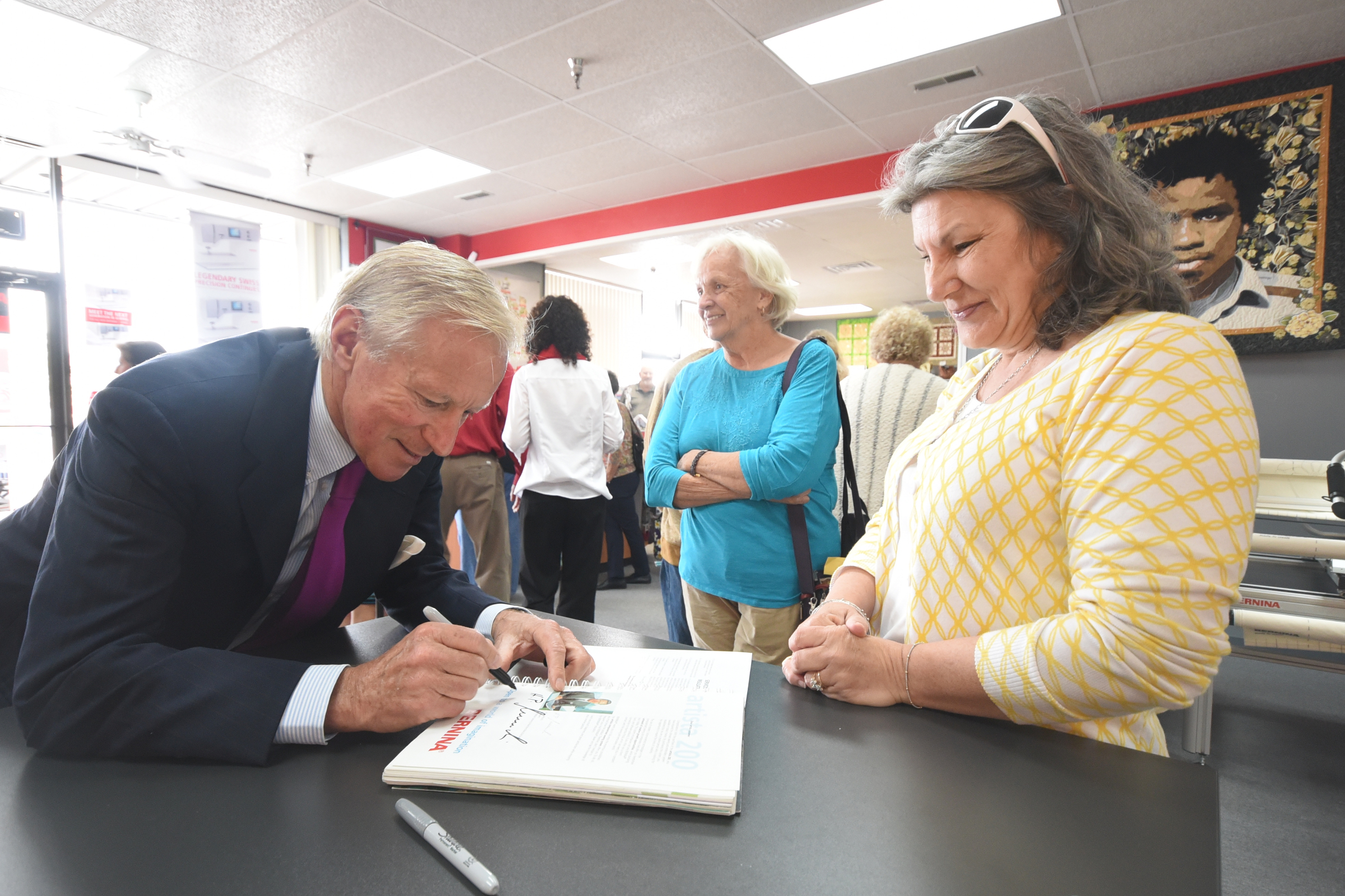Bernina CEO and owner H.P. Ueltschi, left, signs Nancy Cooper's the manual to her Bernina Artista sewing machine inside Bernina Sew N Quilt Studio on Shallowford Road. Phyllis Gatto, center, waits to meet Ueltschi, who picks a couple of U.S. cities each year to visit from his home in Switzerland.