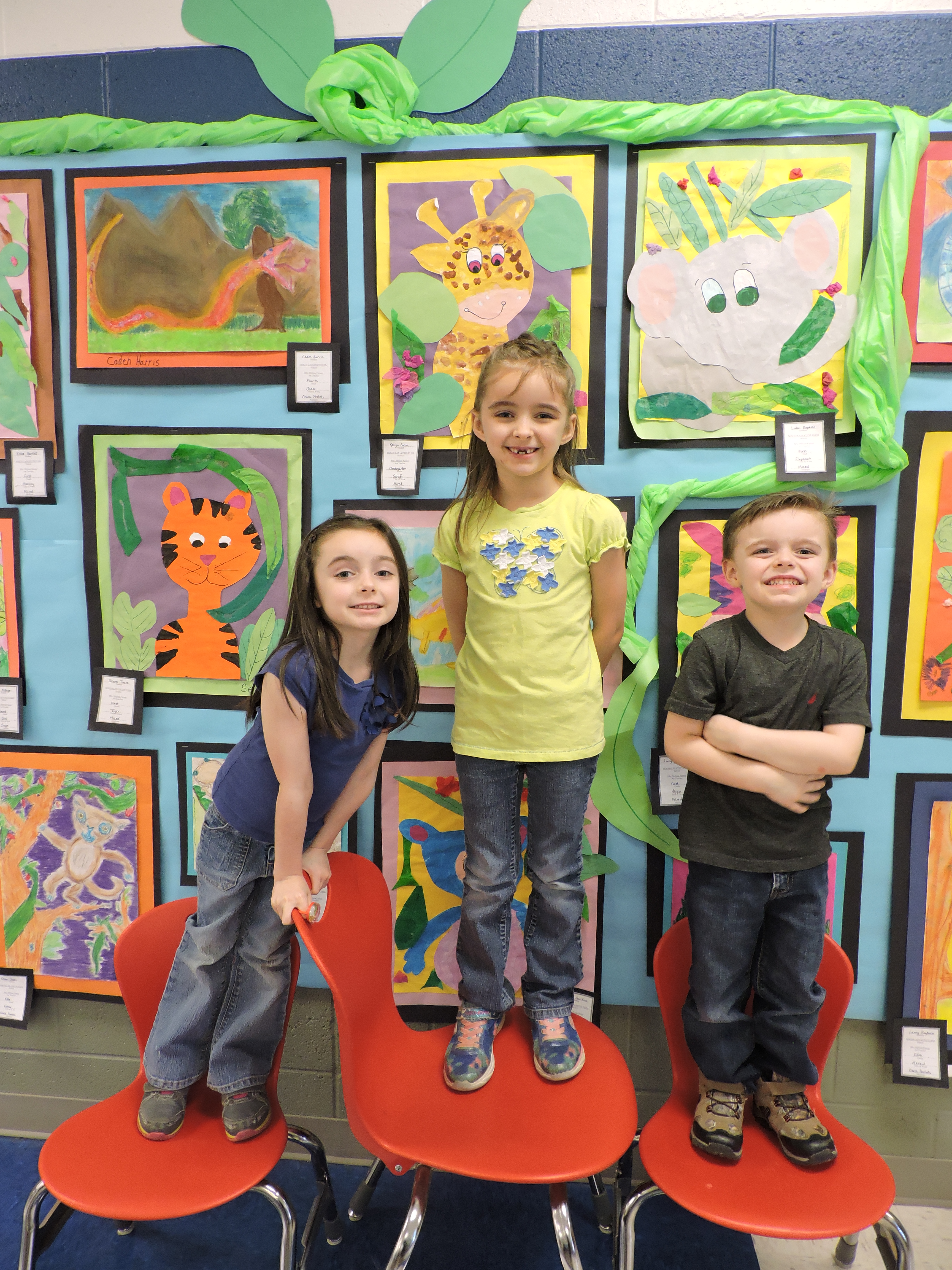 From left are Brailynn Smith, 5, Kailynn Smith, 6, and Elijah Smith, 4, standing beside Kailynn's work of art giraffe at the Artrageous Antic Art Show at Saddle Ridge School.