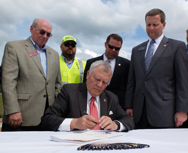 Georgia Gov. Nathan Deal signs the State Budget on Monday as Rep. Tom Dickson, standing left, and Sen. Charlie Bethel, right, look on with other on an Interstate 75 entrance ramp Monday in Dalton Georgia.