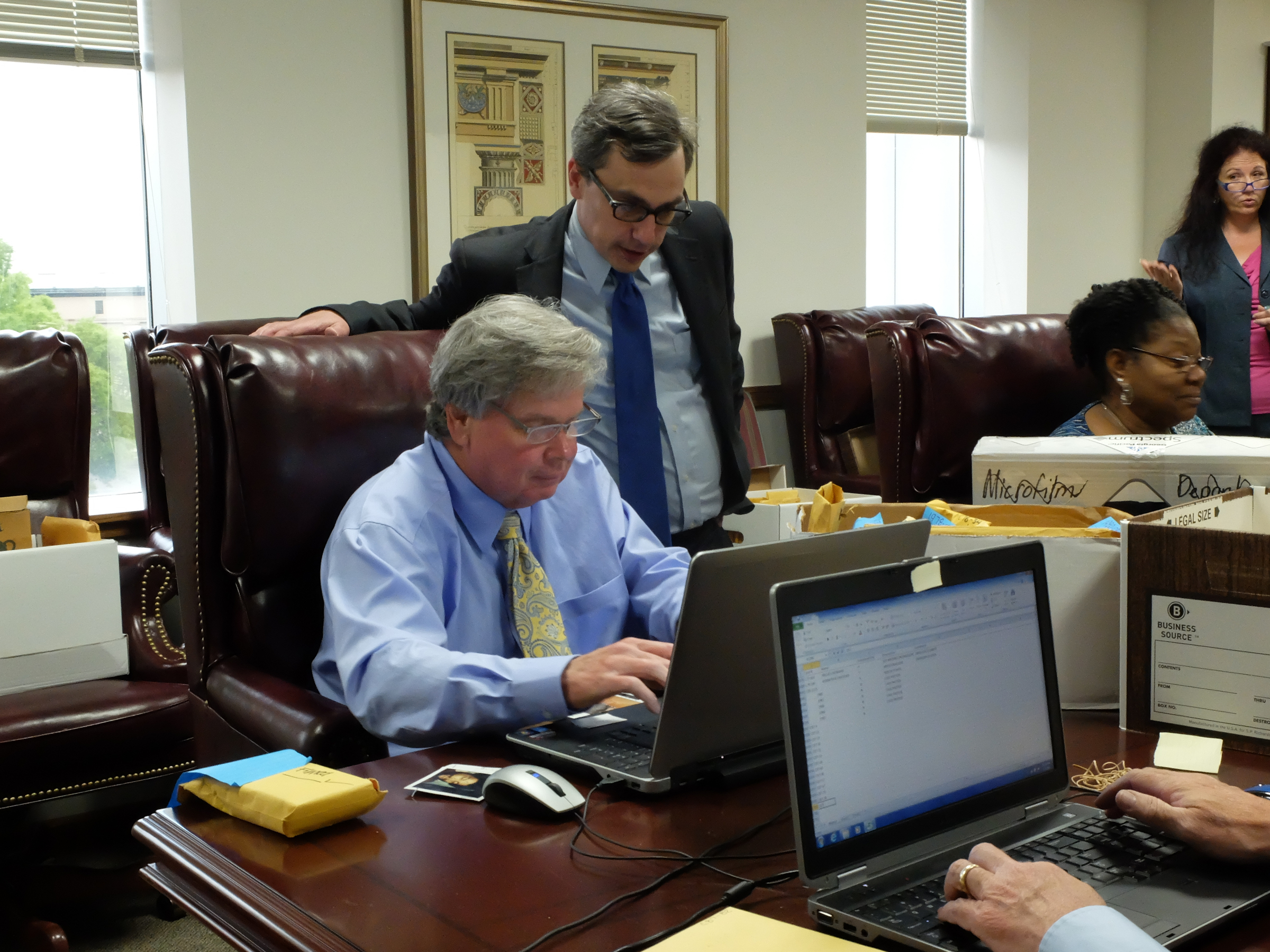 Attorney General Neal Pinkston, top center, stands over senior Hamilton County Auditor Harry Mansfield as he looks at cold case photos.