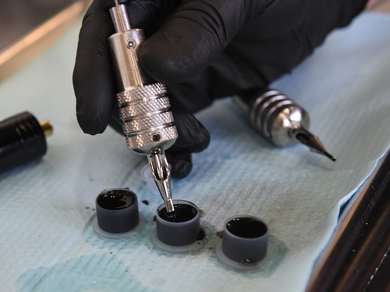 Daniel "Bones" LaLonde, owner of Freedom Tattoo, uses three small plastic containers as he works to cover a previous tattoo on the arm of Craig Silvers on Tuesday, Apr. 26, 2016, in Chattanooga, Tenn. The containers hold, from left, black ink, grey ink, and water used to mix tones in between. 