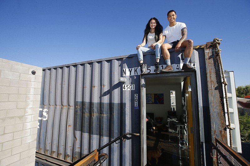 Patrick Tupas, right, with his wife, Maria Real-Tupas, sit on the roof of their shipping container apartment, in Phoenix. In the Containers on Grand project, the apartments are designed in a way that retains the corrugated metal exteriors. Each unit is made of two containers, but inside there are no signs of the cargo hauling days. (AP Photo/Ross D. Franklin)