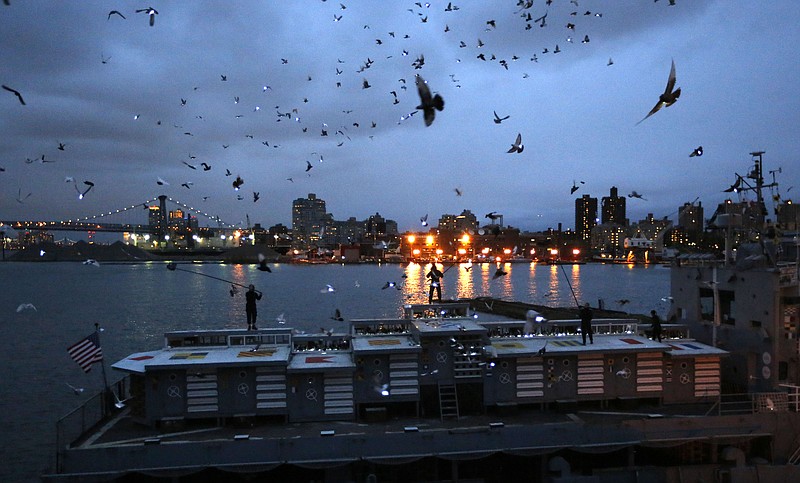 
              Pigeons wearing LED lights fly above their coops on board the Baylander, a decommissioned naval ship docked at the Brooklyn Navy Yard, Thursday, May 5, 2016, in New York. The 30-minute performance was part of artist Duke Riley's "Fly By Night" creation. (AP Photo/Kathy Willens)
            
