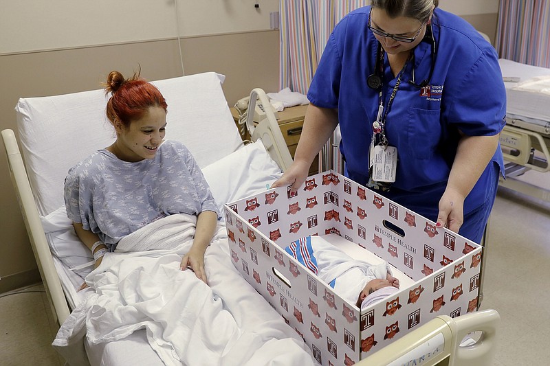 
              Keyshla Rivera smiles at her newborn son Jesus as registered nurse Christine Weick demonstrates a baby box before her discharge from Temple University Hospital in Philadelphia on Friday, May 6, 2016. In an effort to reduce infant mortality the boxes which are functioning bassinets complete with a sheet and mattress as well as essential baby supplies will be given free-of-charge to all mothers who deliver at the hospital. (AP Photo/Matt Rourke)
            