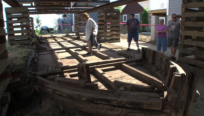 
              Eileen Scanlon, left, steps across a 44-foot wooden boat on Wednesday, May 25, 2016, underneath a home she rents in Highlands, N.J. The 19th-century boat, likely used to transport coal and other goods, sat undisturbed until workers began raising the home  to put it on pilings. (Thomas P. Costello/The Asbury Park Press via AP)  NO SALES; MANDATORY CREDIT
            