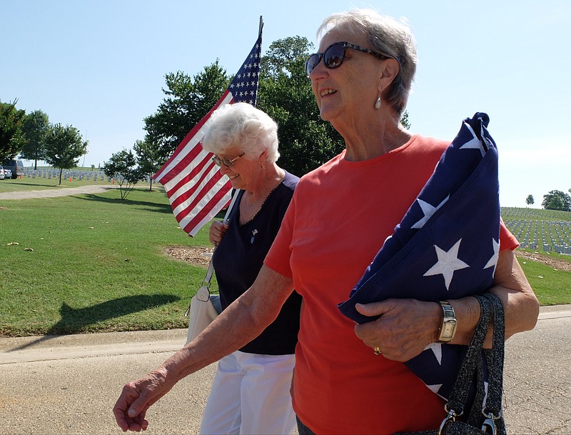 Joana Kelso, of Crossville, carries her husbands flag to the annual Memorial Day program at the Chattanooga National Cemetery on Monday. "I'm bringing it to donate it, so it will fly on one of these poles," Kelso said. Patti Qualls, left, walks to the event with her friend. SSGT Jack Kelso was buried here in Chattanooga just two months ago, according to his wife.