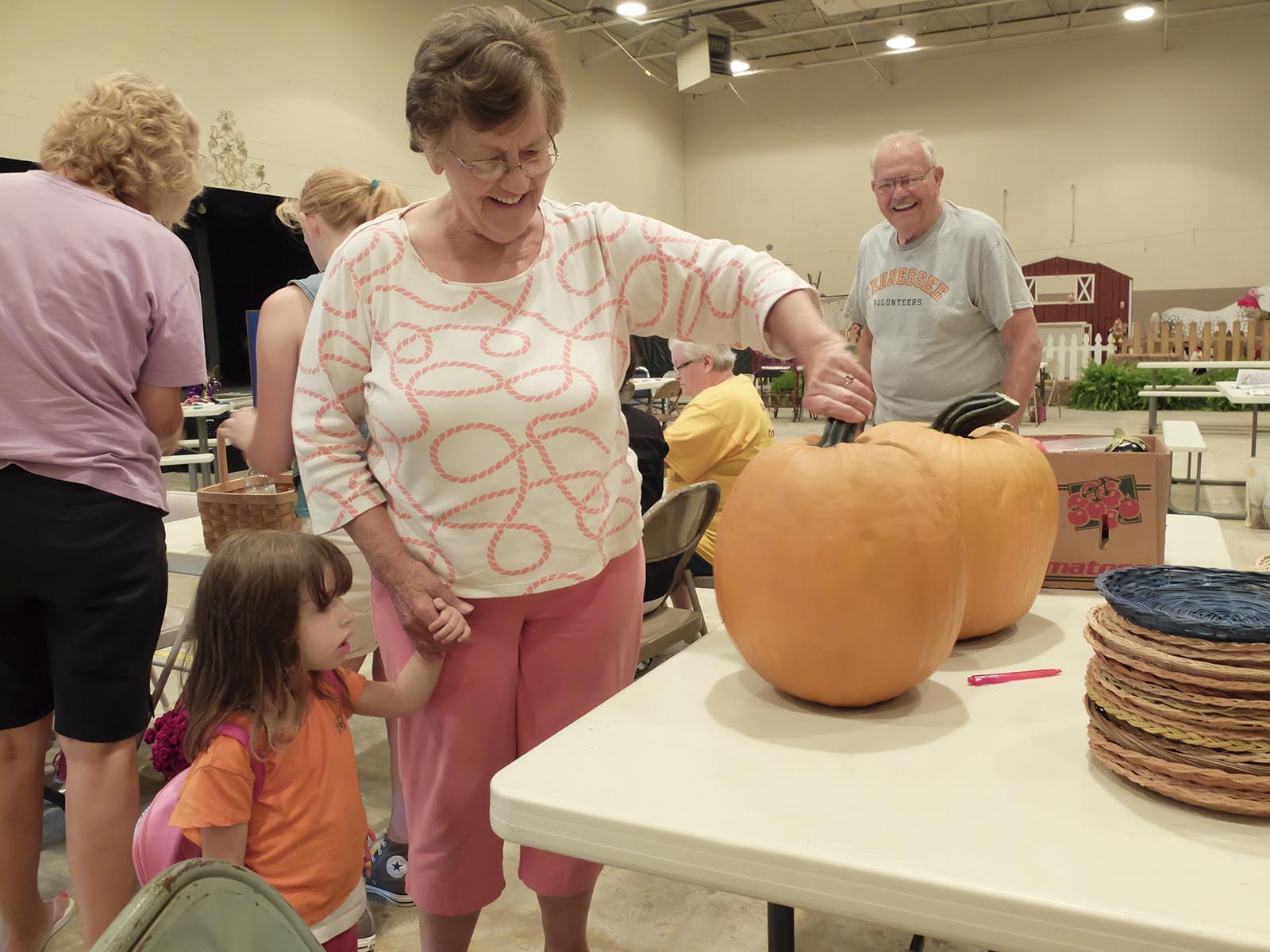 Little Rileigh Keener, 4, lower left, looks at the pumpkins grown by Mary Farley, center. Bill Lowe, right, smiles as they guess at the weight of the produce Monday during registration.  The 88th Annual Sequatchie County Fair opens Wednesday and runs through Monday, Sept. 7.