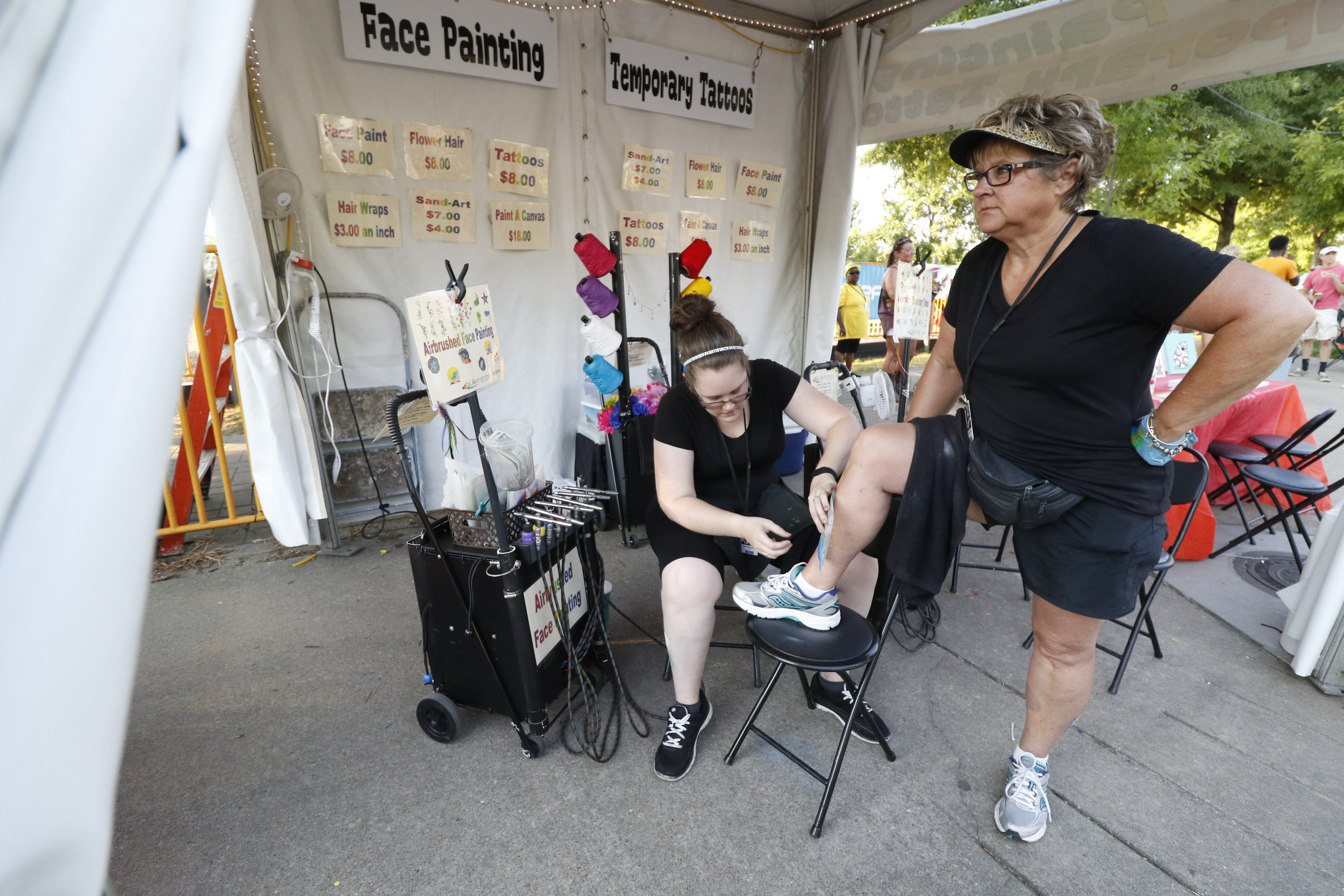Staff Photo by Dan Henry / The Chattanooga Times Free Press- 6/12/16. Megan James with Air illustrations airbrushes a fish scene on Susan LeMaster's leg during the 2016 Riverbend Music Festival in downtown Chattanooga on Sunday, June 12, 2016. This is the 35th year of the festival.