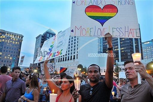 Stacy Timm, from left, Nizam Khan and Fabien Houle, all of Orlando, Fla., hold up signs and candles during a vigil honoring the victims of a mass shooting at Orlando's nightclub Pulse, as they gather at the Dr. P. Phillips Center for the Arts in Orlando on Monday, June 13, 2016. (Craig Rubadoux/Florida Today via AP) 