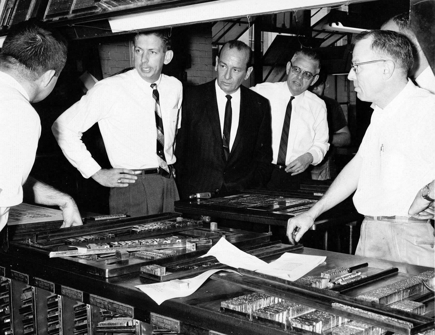 Editor Lee Anderson, second from left, coordinates the production of the newspaper on the day of the assassination of President John F. Kennedy. Also pictured in the November 22, 1963 photo are, from left; a unidentified newspaper employee, Mr. Anderson, City Editor Julius Parker, Circulation Manager Bill Hoback, and page one designer Bud Davis.