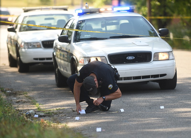 A Chattanooga police officer takes a closer look Monday afternoon at shell casings on Monroe Street near the intersection with Arlington Avenue.