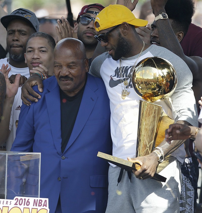 Former Cleveland Brown' Jim Brown, left, passes the Larry O'Brien NBA Championship Trophy to LeBron James during a rally, Wednesday, June 22, 2016, in Cleveland. The Cavaliers made history by overcoming a 3-1 deficit to beat the Golden State Warriors in the NBA Finals and end the city's 52-year drought without a professional sports championship. (AP Photo/Tony Dejak)