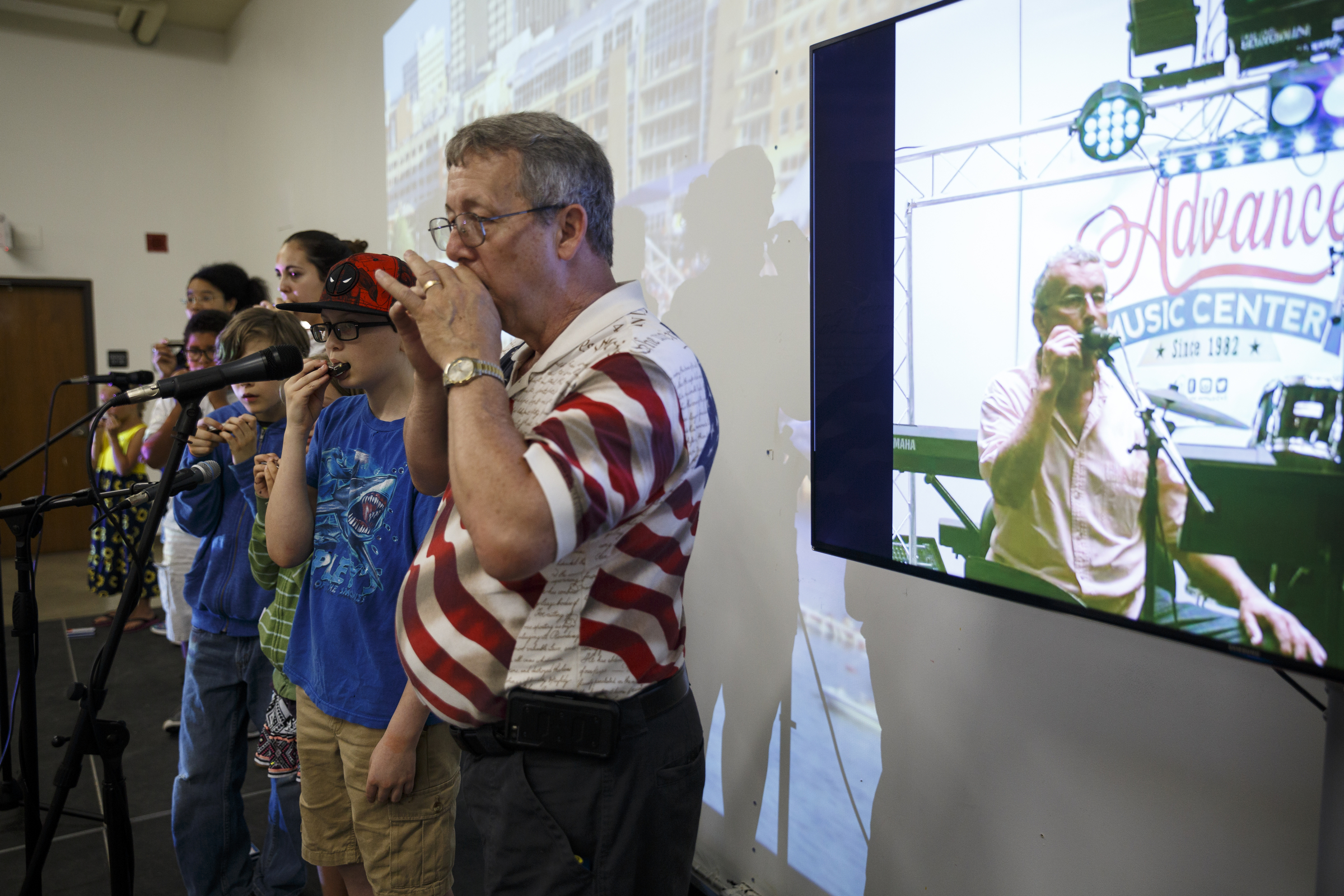 Ray Long, left, and others play along as musician Mark LaVoei gives a harmonica lesson on a screen from Burlington, Vermont, at the Chattanooga Public Library on Tuesday, June 21, 2016, in Chattanooga, Tenn. For Make Music Day, the library hosted interactive events that connected digitally to Burlington.
