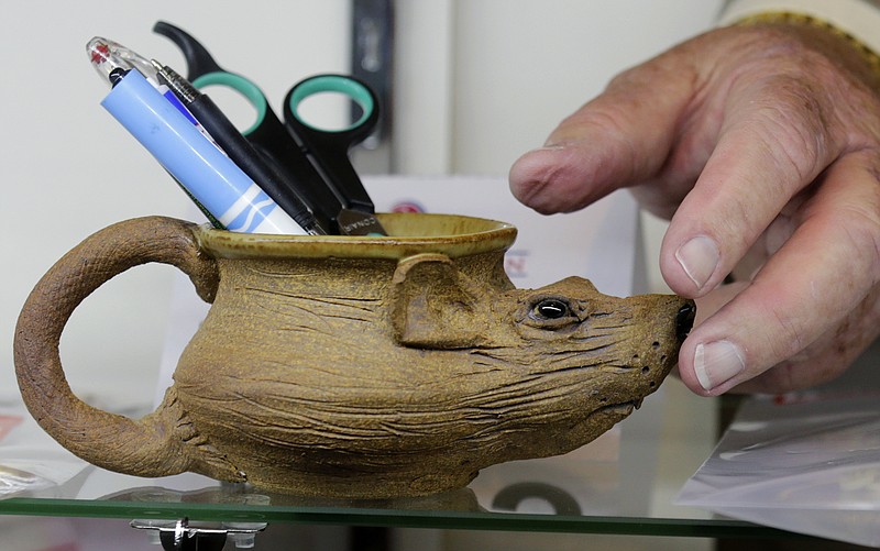 
              Auctioneer Bob Sheehan reaches for a pottery mug, in the shape of a rat, which contains pens, that are among items belonging to James "Whitey" Bulger and Catherine Greig, which will be auctioned off this weekend at the Boston Convention Center, Friday, June 24, 2016, in Boston. The proceeds will be divided among the families of Bulger's victims. (AP Photo/Charles Krupa)
            