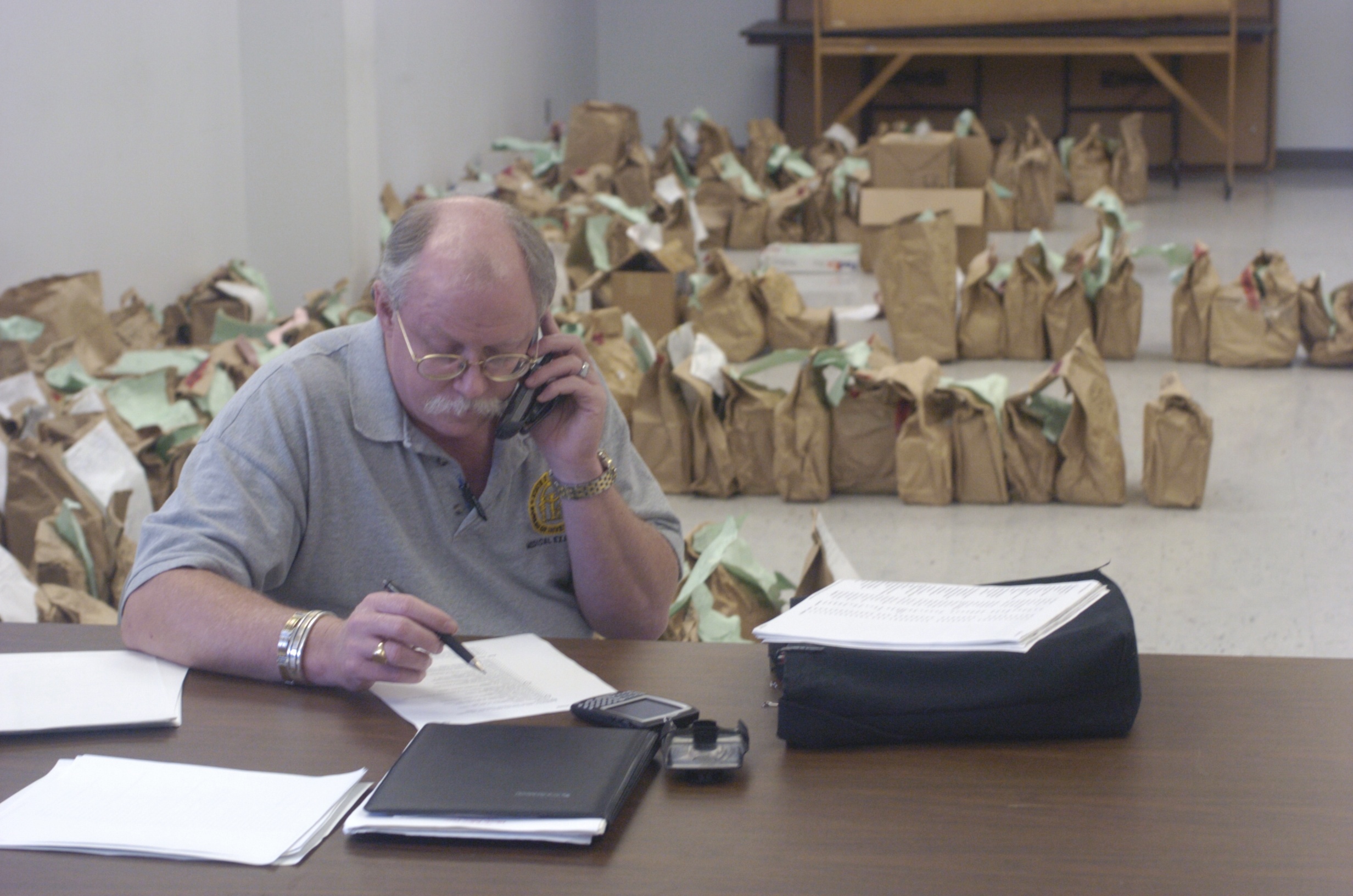 Staff Photo by John Rawlston             Dr. Kris Sperry of the Georgia Medical Examiner's office talks on the telephone Wednesday as he sits in a room with evidence bags from the Tri-State Crematory investigation. Family members were allowed to reclaim the bags, most of which contain bogus cremains.