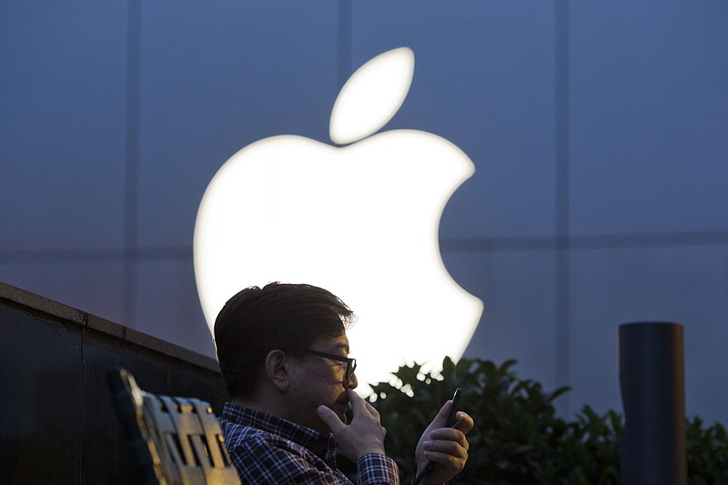 
              FILE - In this Friday, May 13, 2016 file photo, a man uses his mobile phone near an Apple store logo in Beijing, China. A Beijing court said in an online statement Thursday, June 30, 2016, that Apple is being sued by a subsidiary of China's broadcasting regulator over a propaganda film more than 20 years old, in the latest legal wrangling for the tech giant in China in recent weeks. (AP Photo/Ng Han Guan)
            