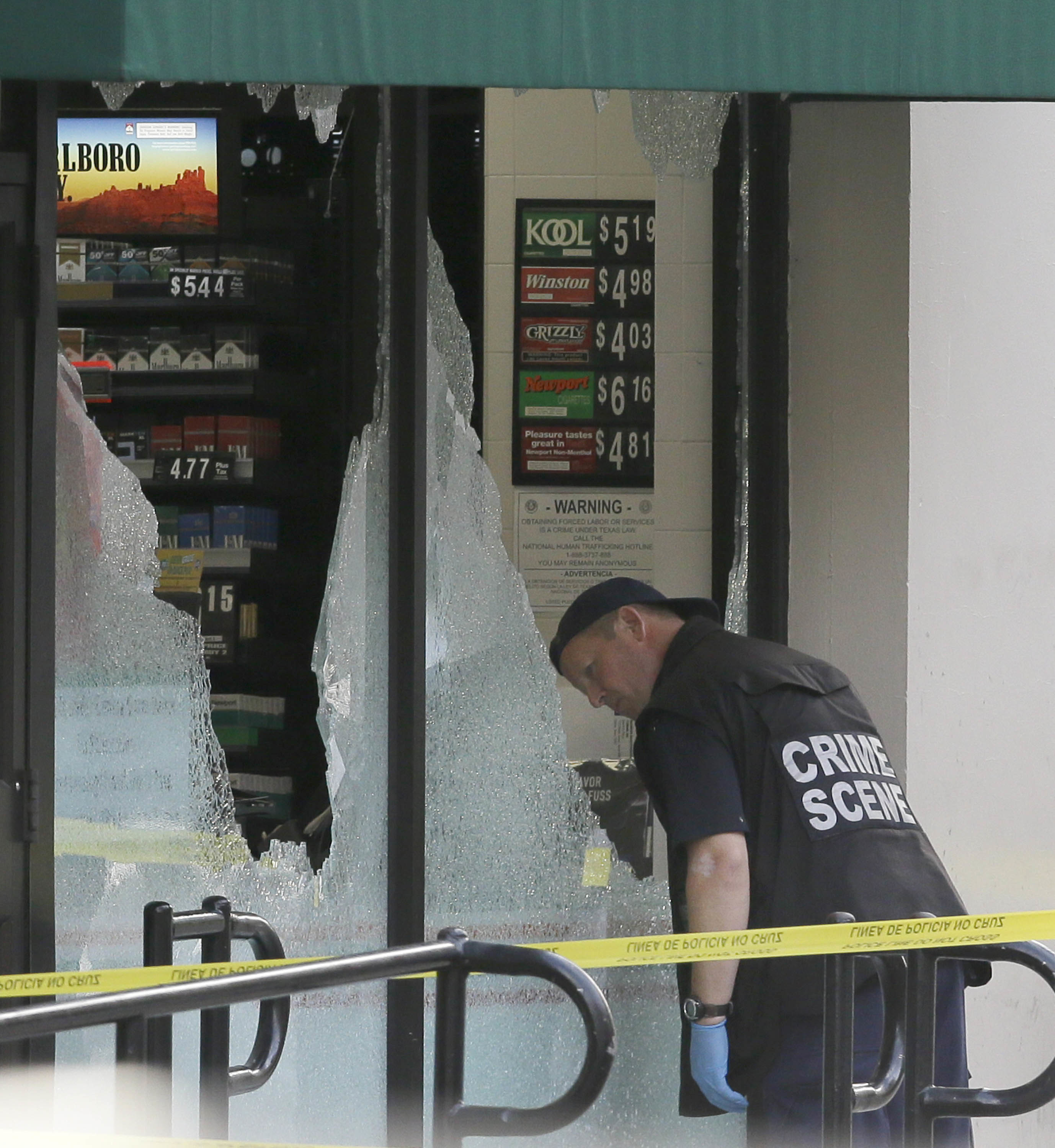 A crime scene investigator looks a shot out windows after a shooting in downtown Dallas, Friday, July 8, 2016. Snipers opened fire on police officers in the heart of Dallas during protests over two recent fatal police shootings of black men. (AP Photo/LM Otero)
