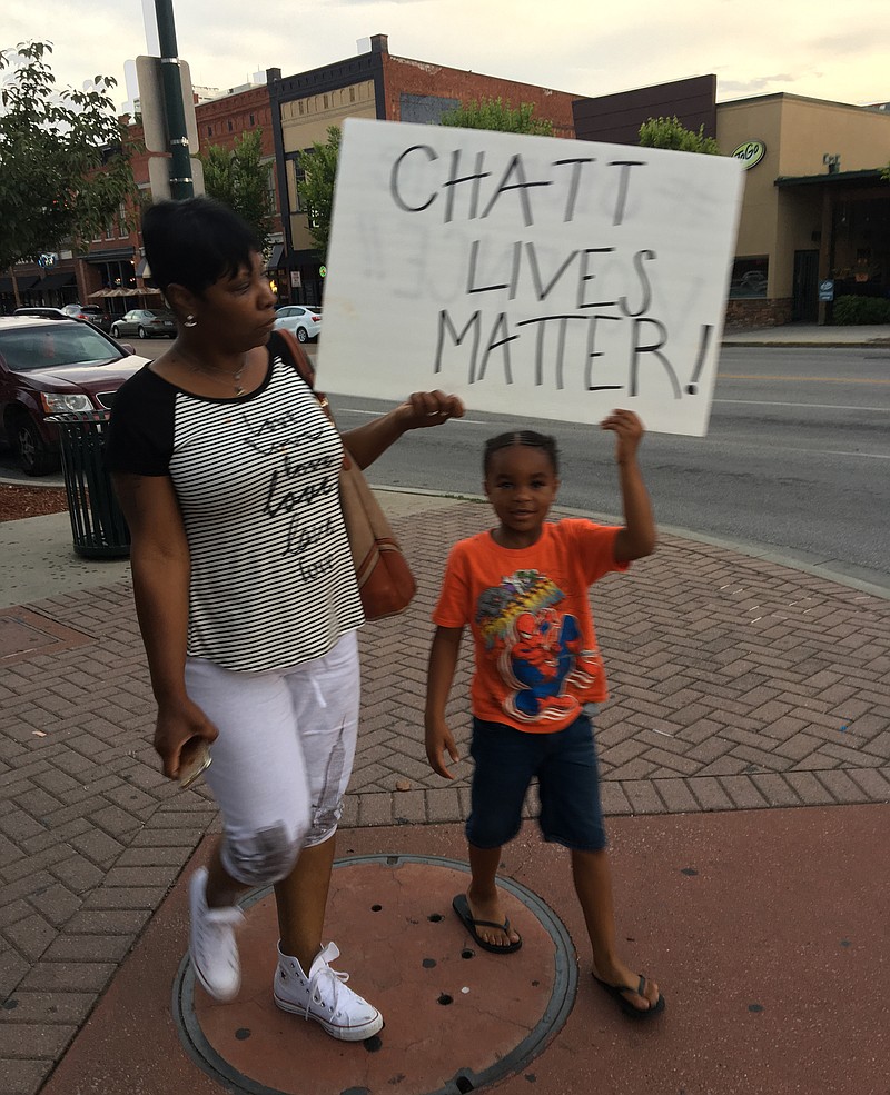 A woman and child participating in a march on Sunday in downtown Chattanooga hold a sign as they prepare to cross a street.