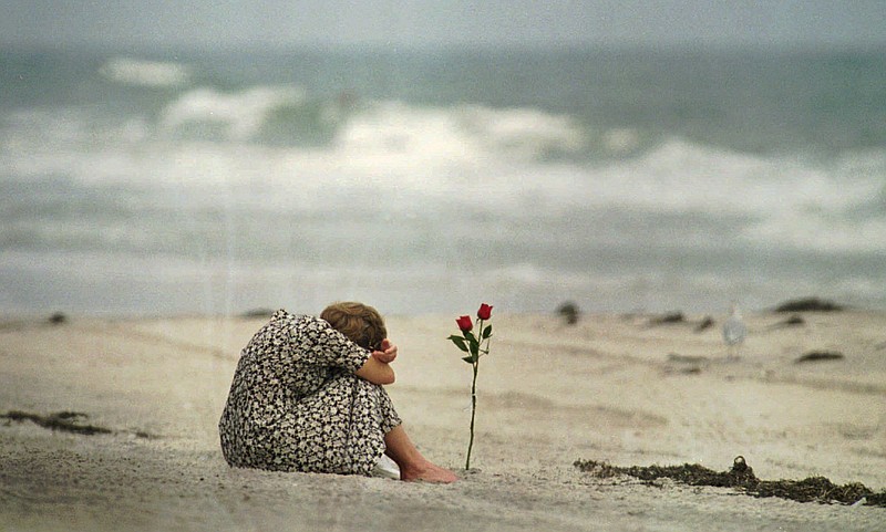 In this July 26, 1996, file photo, a woman sits near a rose she placed in the sand at Smith Point Park Beach in Shirley, N.Y. , as she mourns the loss of some of her friends who were on the flight crew for TWA Flight 800. Twenty years after the Boeing 747 exploded in a fireball off Long Island, killing all 230 aboard, the passage of time has been a salve for some, but others will never get over the heartache.