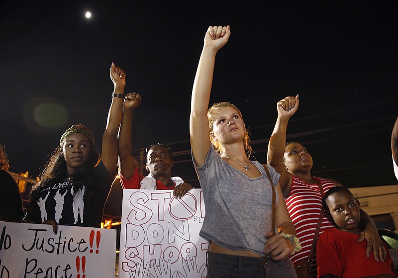 
              Ella Carr, center, of Austin, Texas, puts her fist up during live music at a night rally in honor of Alton Sterling, outside the Triple S Food mart in Baton Rouge, La., Monday, July 11, 2016. Sterling was shot and killed last Tuesday by Baton Rouge police while selling CD's outside the convenience store. (AP Photo/Gerald Herbert)
            