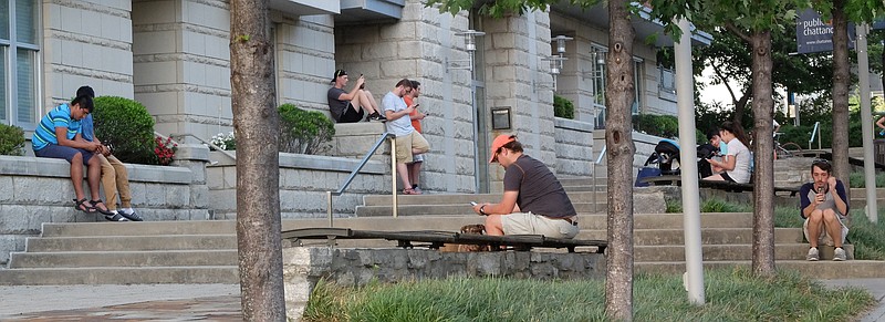 PokemonGo players look at their cell phones in the E. 1st Street walkway to the Walnut Street Bridge between to condominium buildings.