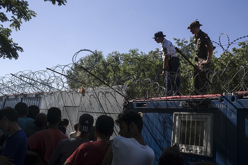 
              Hungarian police and army officers oversee the distribution of food as people queue inside a migrant camp at Serbia's border with Hungary, in Horgos, Serbia, Monday, July 11, 2016. In what appears to be another refugee crisis in the making in Europe, the numbers are surging at camps on Serbia’s border with EU country Hungary. The numbers have been growing since last week, when Hungary introduced forced deportations of migrants caught within 8 kilometers (5 miles) of border fences. (AP Photo/Marko Drobnjakovic)
            