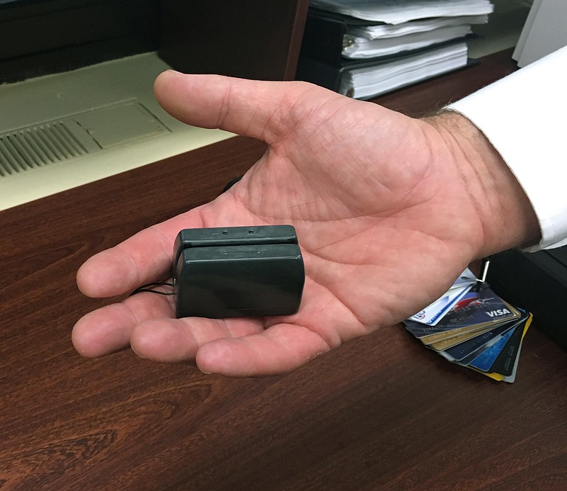 In this Dec. 17, 2015 photo, a New York City Police detective holds a credit card skimmer that was used by a street gang to copy metadata from legitimate credit cards for use in the manufacture of counterfeit cards and possibly identity theft. A new trend is emerging that shows street crews and local gangs giving up more traditional activities like gun point robberies or drug running for more white-collar varieties of crime like identity theft or credit card fraud. (AP Photo/Colleen Long)