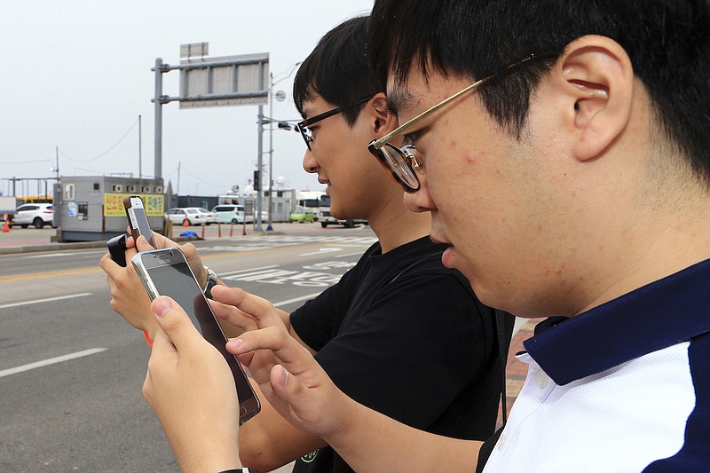 
              In this July 13, 2016 photo, two South Koreans play the Pokemon Go game with their mobile phones in Sokcho, South Korea. The seaside South Korean city of Sokcho is enjoying a surge of visitors who are wandering the streets at all hours as they look at their smartphones. It appears to be the only place in the country where Pokemon Go players can chase the mobile game's virtual monsters. (Lee Jong-hun/Yonhap via AP)
            