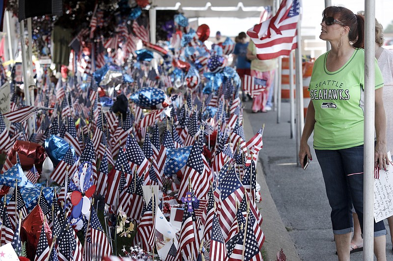 Leslie Robertson, who traveled from Port Angeles, Wash., a year ago, carries a sign to the temporary Lee Highway memorial for the five servicemembers who died in a terrorist attack at the Naval Operational Support Center and Marine Corps Reserve Center on Amnicola Highway.