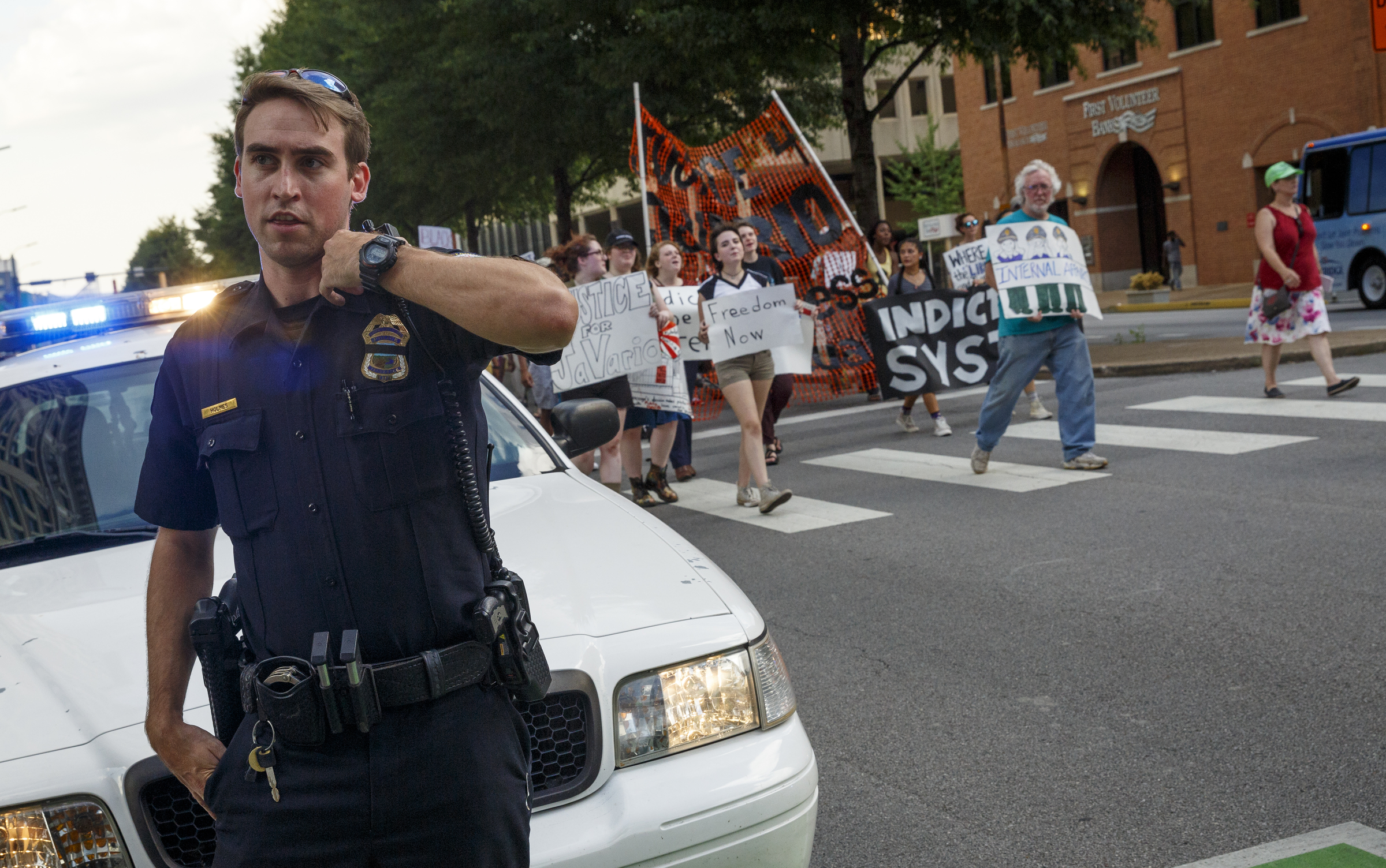 Chattanooga Police Officer Holmes blocks traffic on Broad Street as protesters cross at 8th Street during a Black Lives Matter protest Thursday, July 21, 2016, in Chattanooga, Tenn. Protesters marched from Miller Park to the Tennessee Aquarium and back, stopping and blocking numerous intersections along the route.