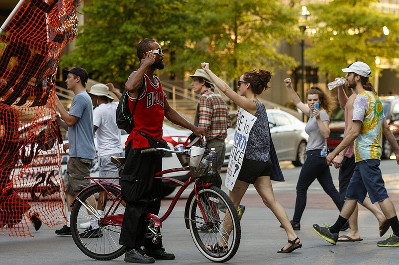 A passerby on a bike salutes protesters as they cross Martin Luther King, Jr., Boulevard during a Black Lives Matter protest Thursday, July 21, 2016, in Chattanooga, Tenn. Protesters marched from Miller Park to the Tennessee Aquarium and back, stopping and blocking numerous intersections along the route.