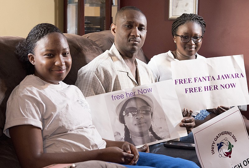 
              FILE - In this June 14, 2015 file photo, Ebrima Jawara poses with his daughters Sarah, left, and Aminata, while holding a picture of his wife Fanta Darboe Jawara, who is being held in Gambia's notorious Mile 2 Central Prison, as they anxiously await her return to their Frederick, Md. home. Jawara says his wife, a naturalized U.S. citizen, has been wrongfully sentenced to three years imprisonment in Gambia following her arrest during an anti-government protest where her husband says she was a bystander during a visit to her homeland. (Bill Green/The Frederick News-Post via AP, File)
            